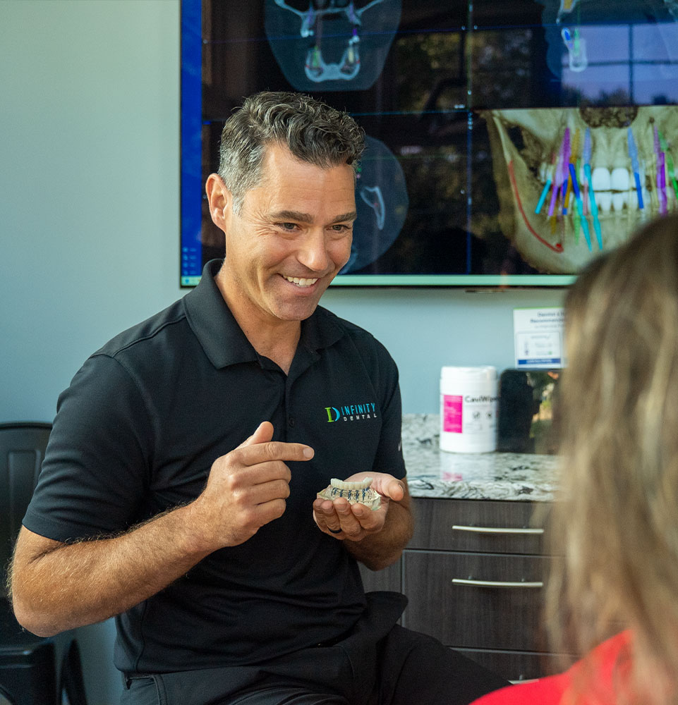 doctor showing patient a full arch dental model during patient implant consultation