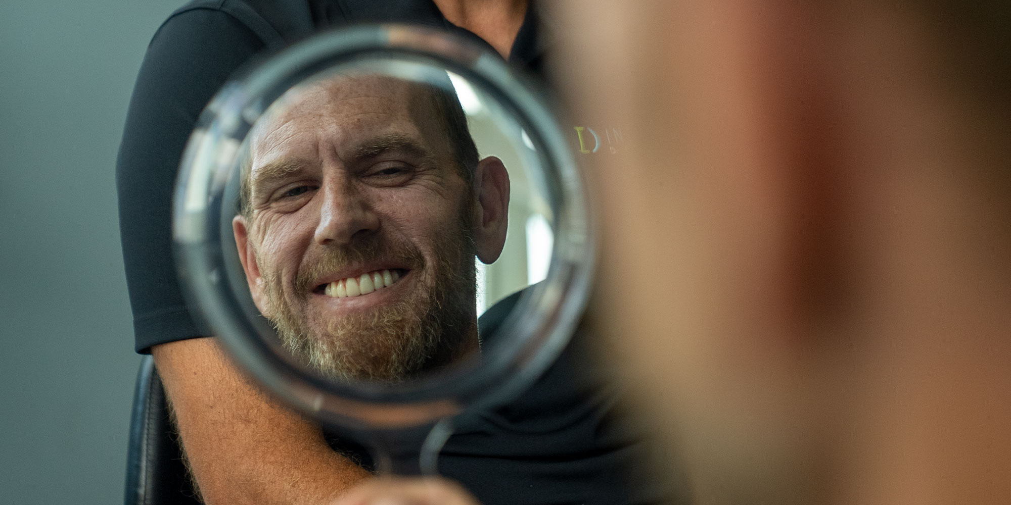 patient smiling brightly while looking in a hand hield mirror within the dental center