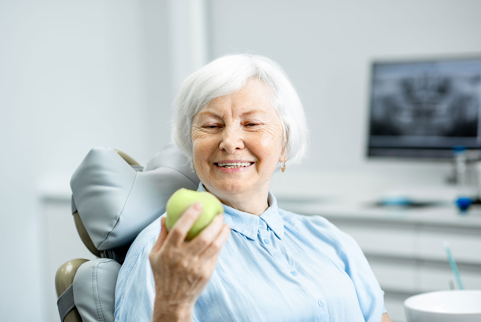 Portrait of a beautiful senior woman with healthy smile holding green apple at the dental office