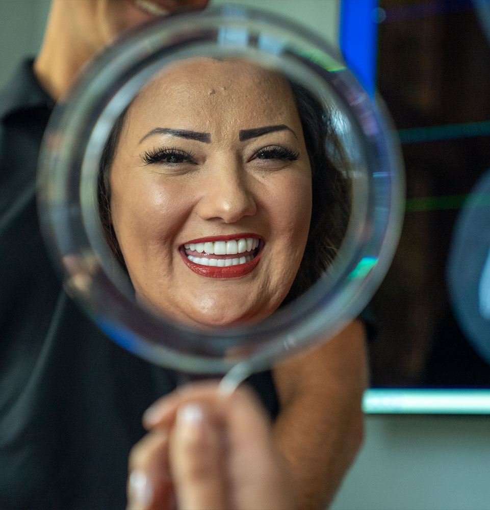 patient smiling brightly while looking at a handheld mirror after their dental procedure