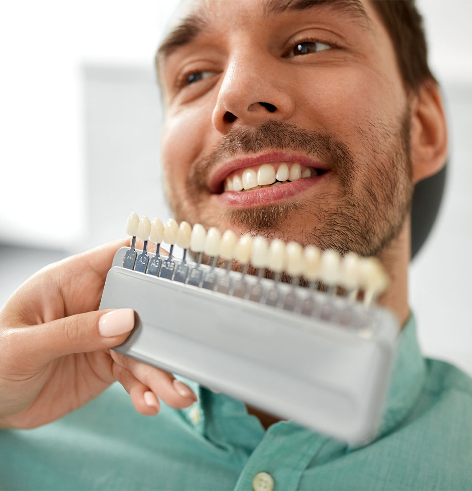 dentist with tooth color samples choosing shade for male patient teeth at dental clinic